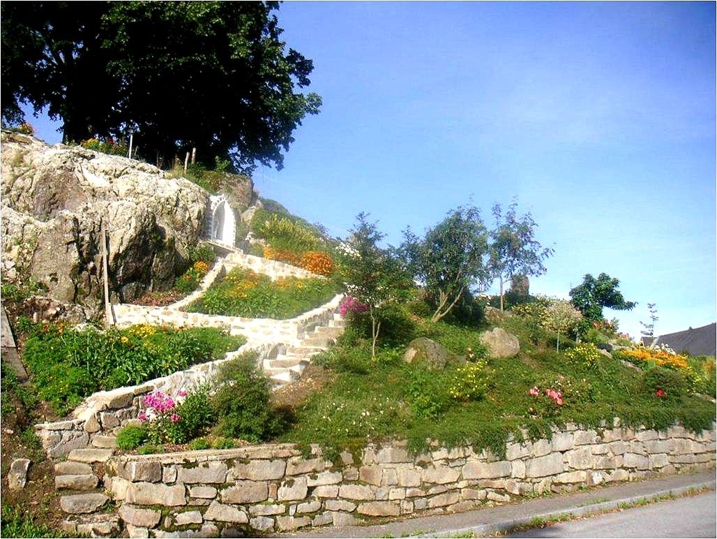 Rock garden with flowers and steps, surrounded by trees.