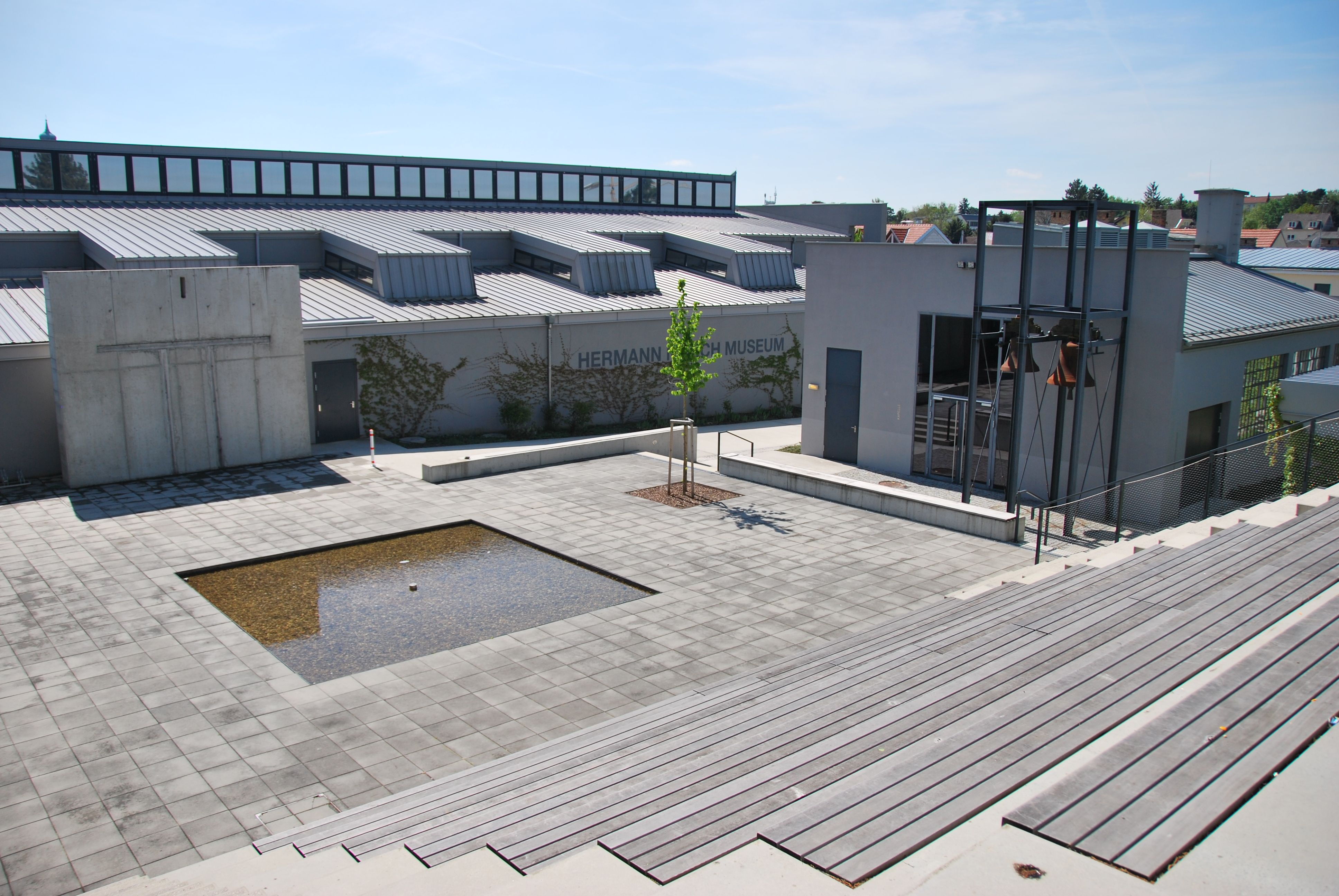 Exterior view of the Hermann Nitsch Museum with modern design and a small water basin on the piazza.