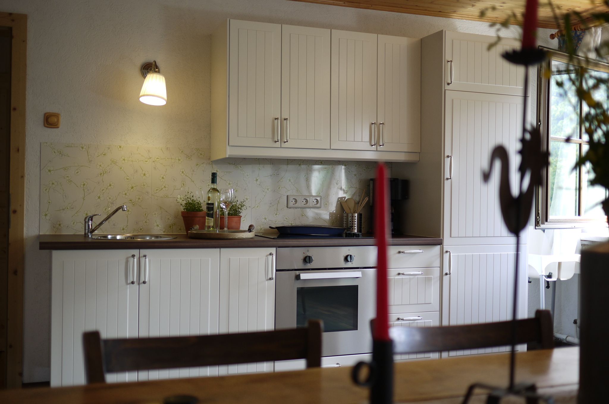Kitchen with white cupboards, stove and sink, decorated with plants and a bottle of wine.