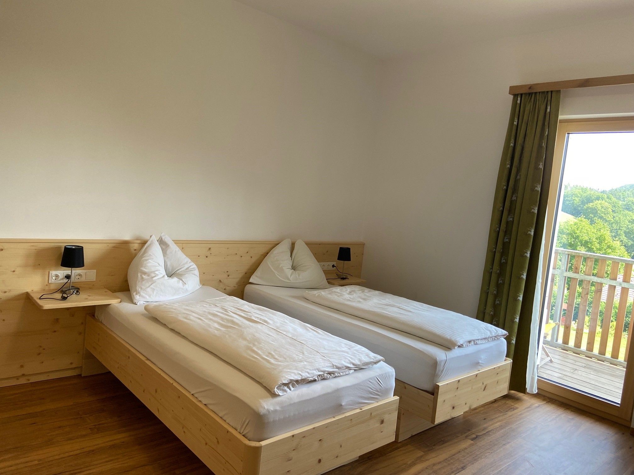 Double room with wooden floor, two single beds, bedside lamps and a balcony with a view of the countryside.