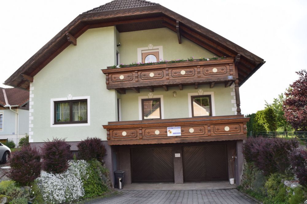 A two-story house with a green facade and wooden balconies, surrounded by well-tended gardens.