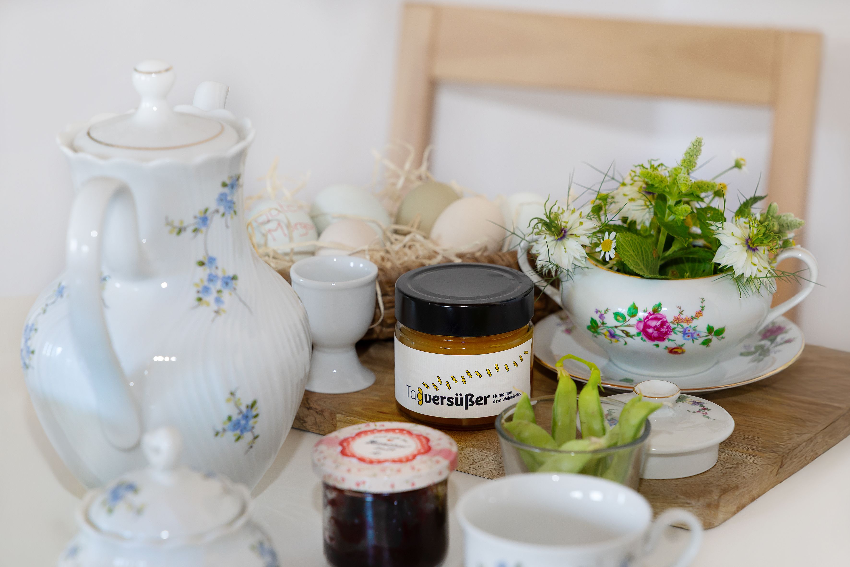 Breakfast table with teapot, jar of honey, jam, eggs and flowers.