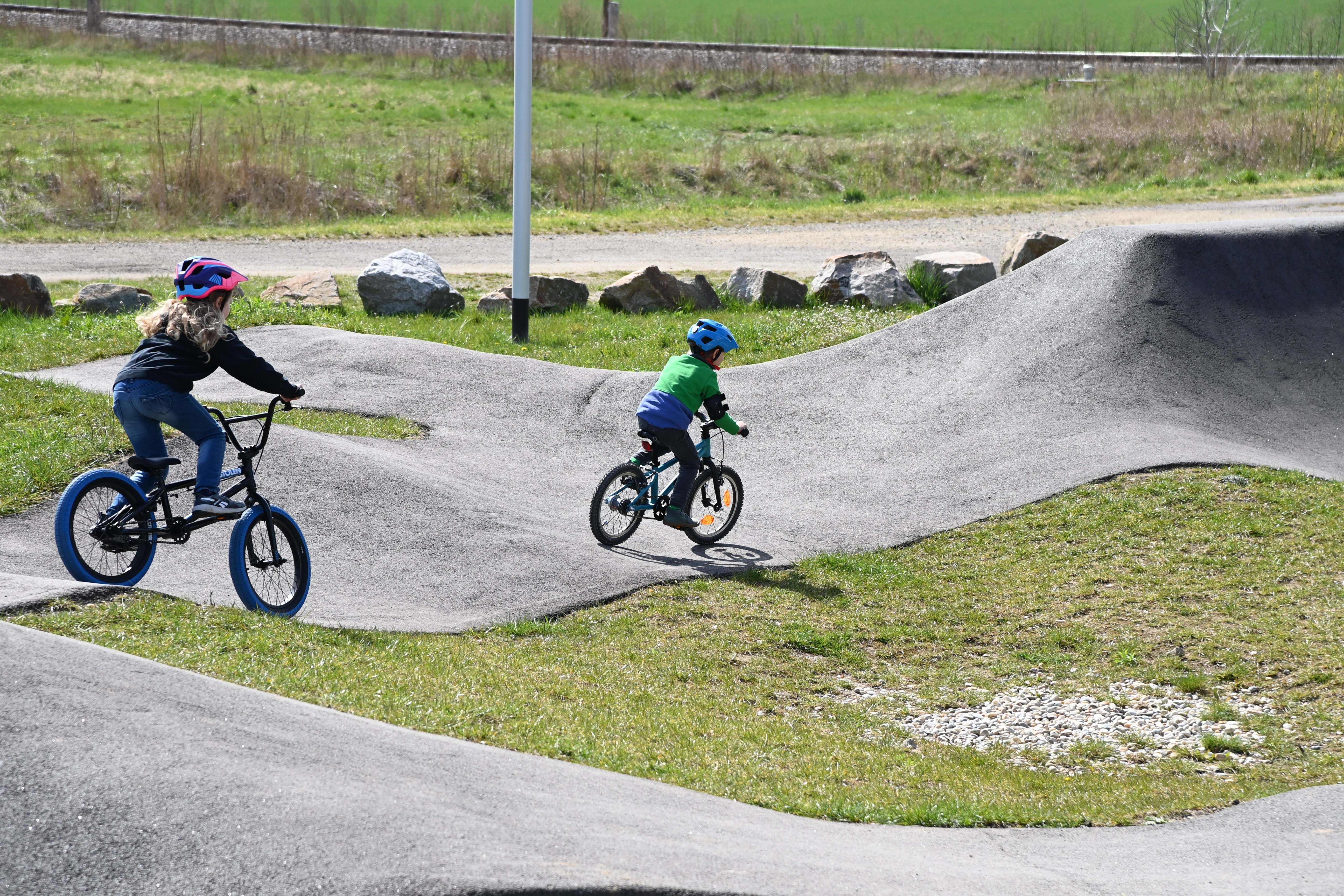 Two children riding bikes on an outdoor pump track.