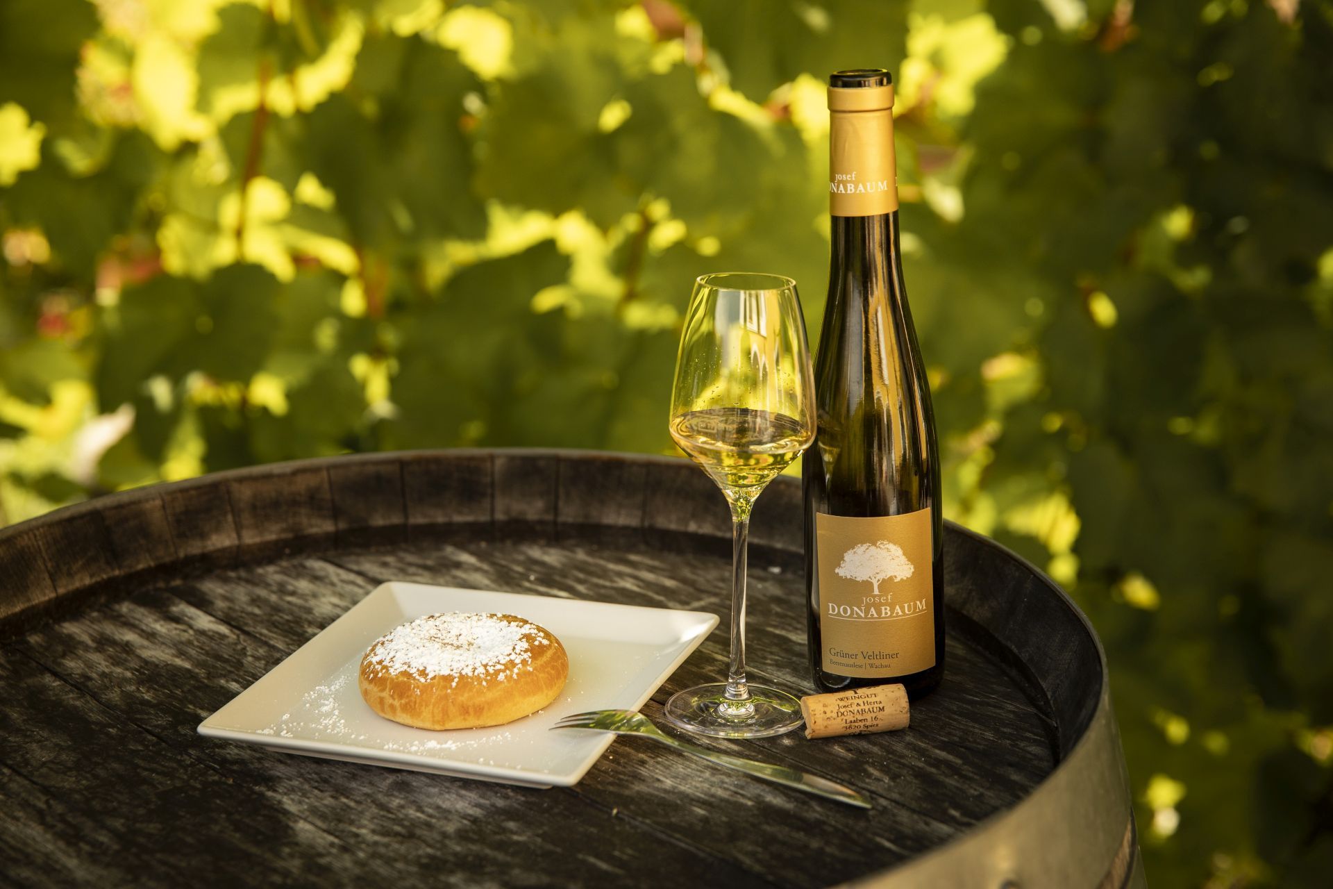 Wine bottle and glass with pastries on a barrel outside.
