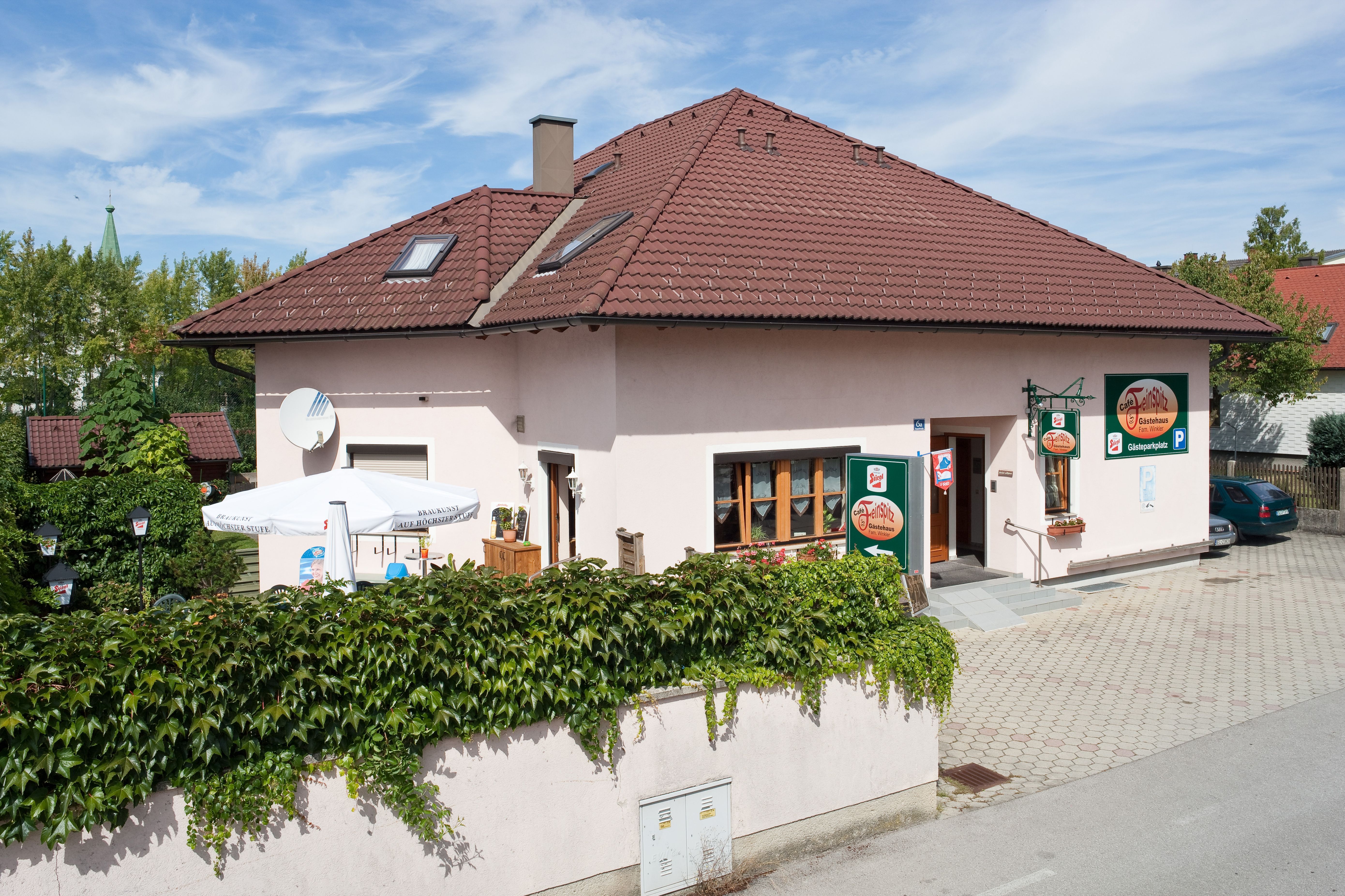 A guest house with a red roof and terrace, surrounded by green vegetation.