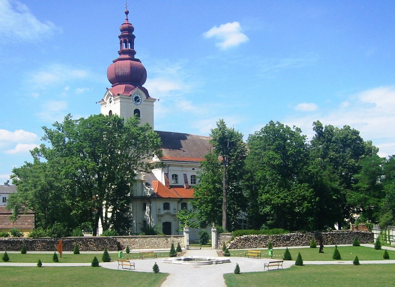 Baroque church with red tower and garden in the foreground.