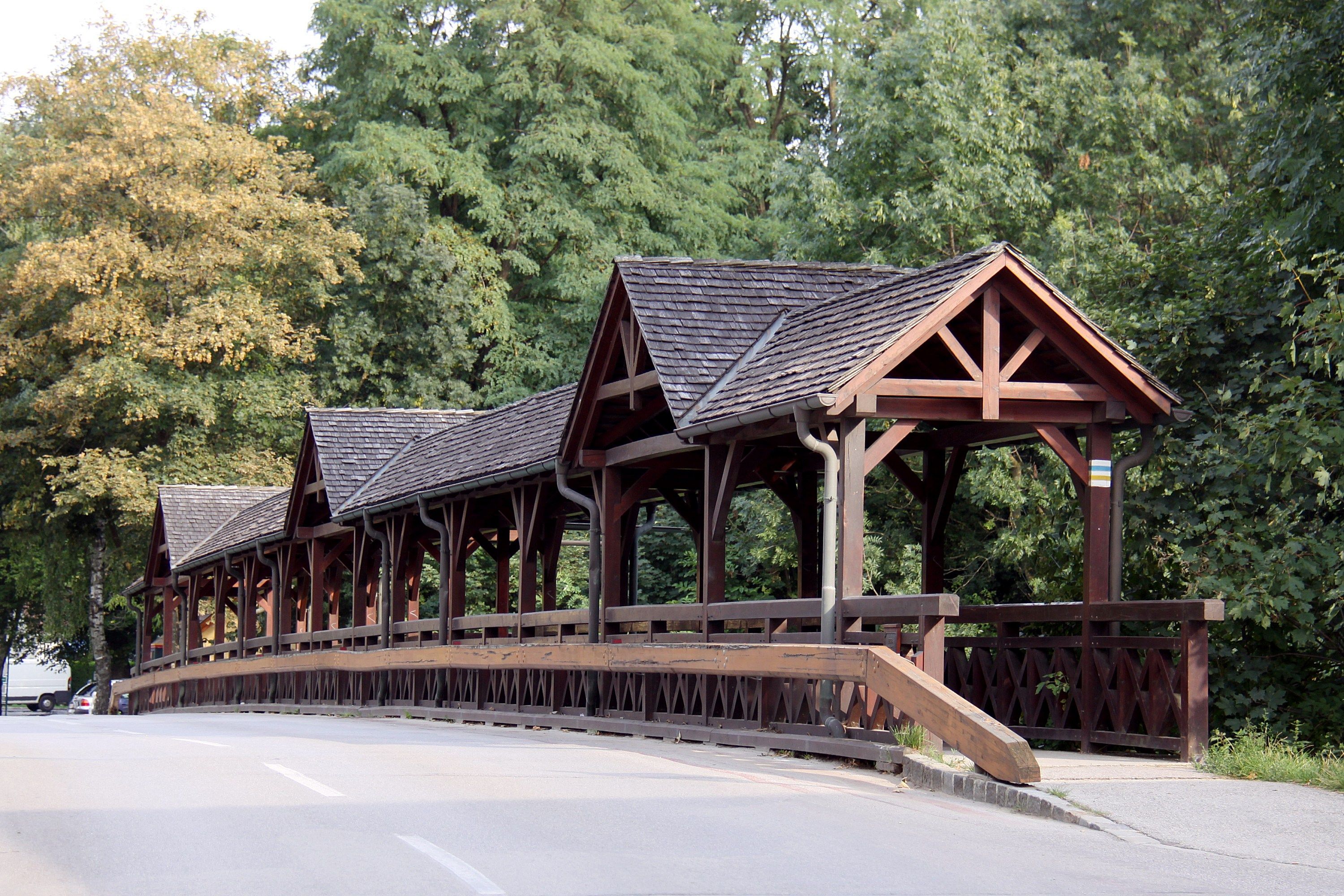 Wooden bridge with covered walkway in a green setting.