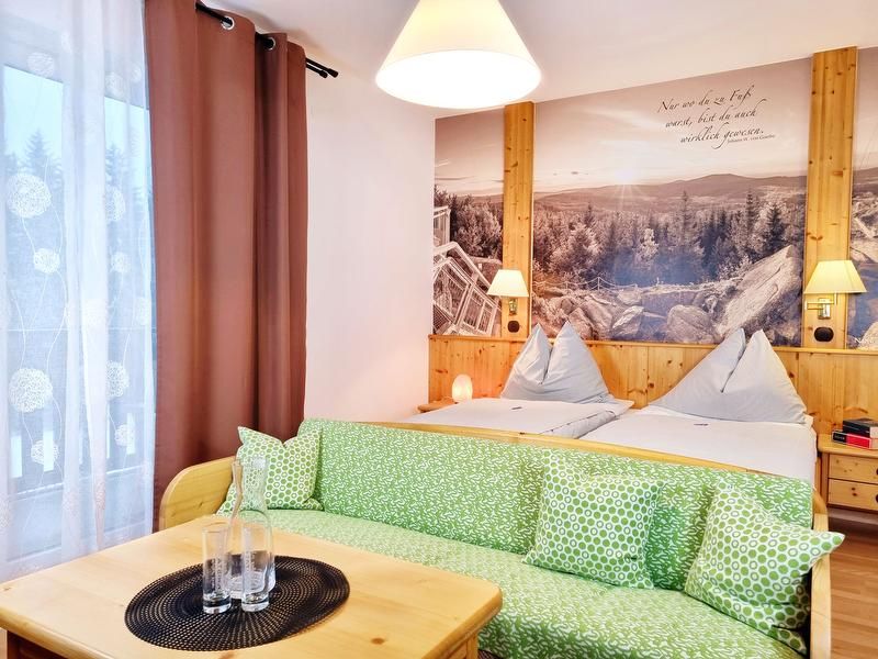 Cozy double room with two beds, green sofa and large mural of a landscape.