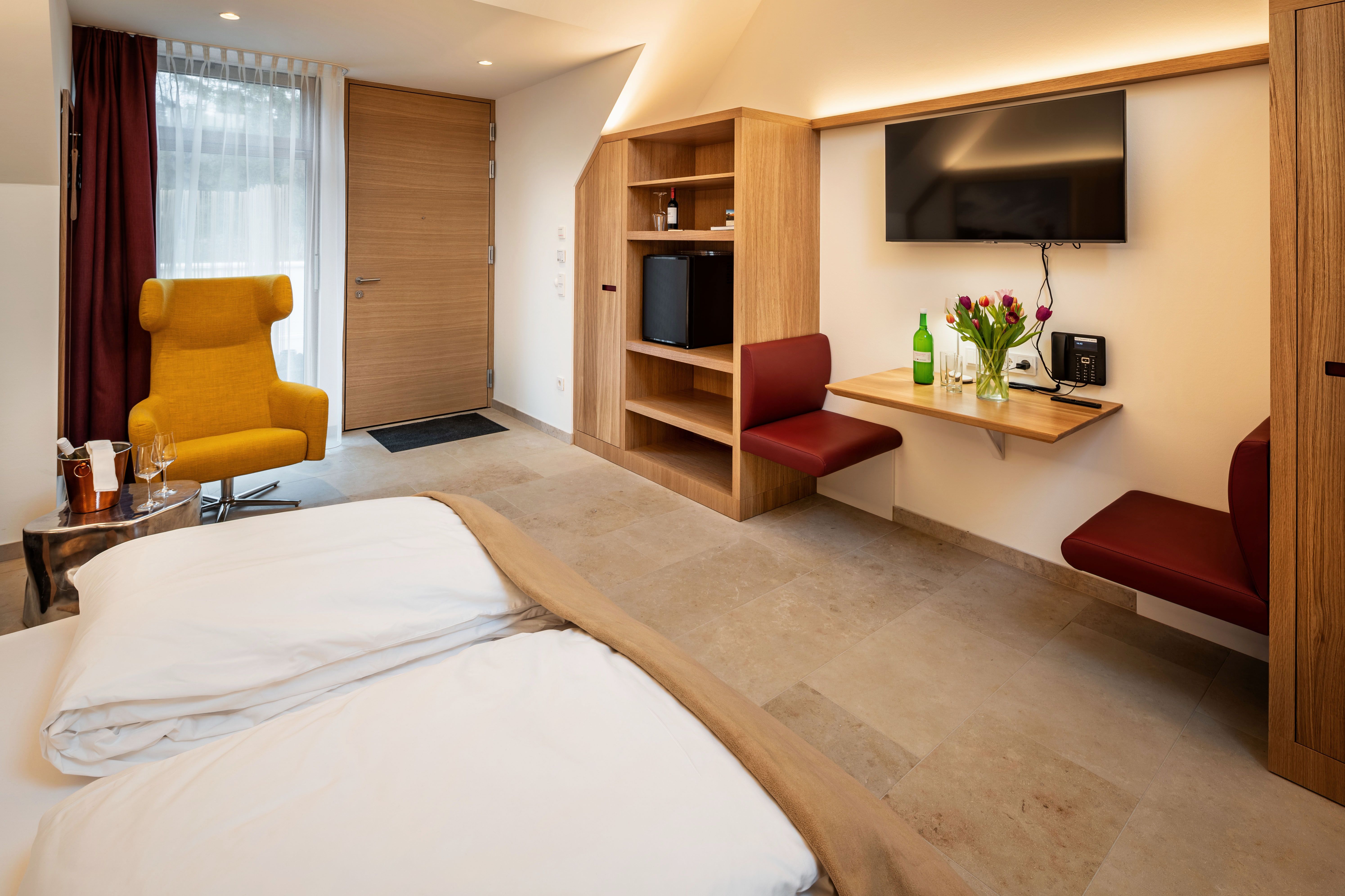 Modern hotel room with yellow armchair, wooden furniture and flowers on a table.