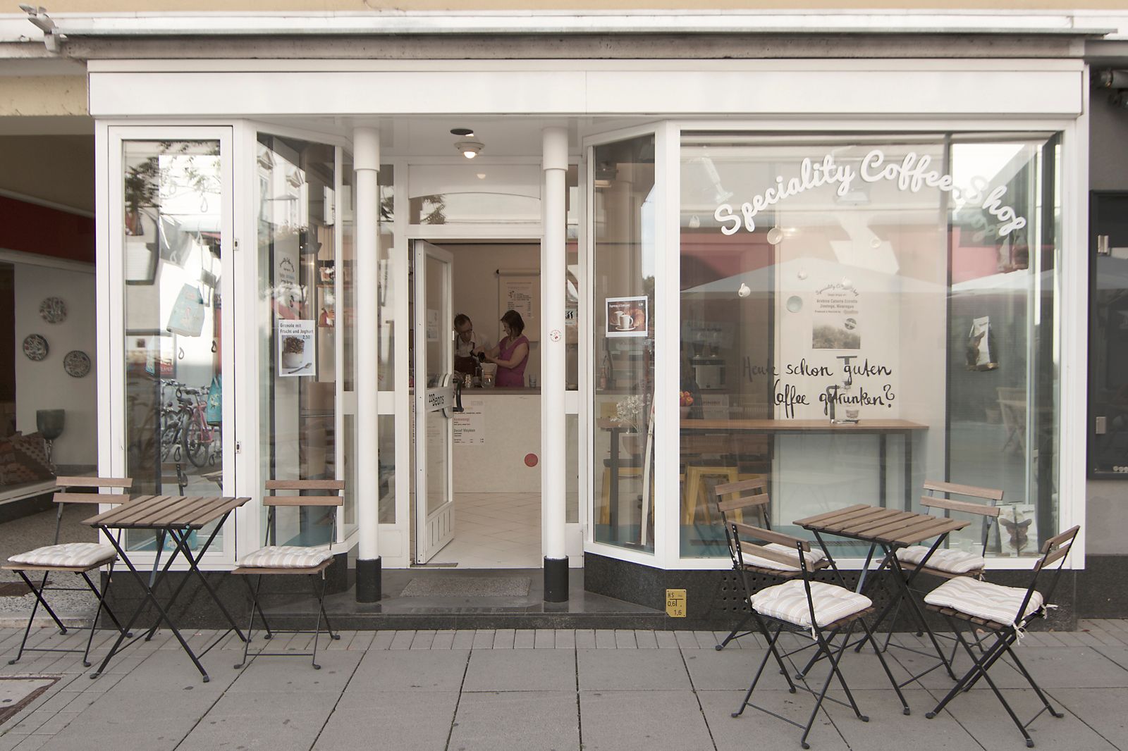 Exterior view of a café with tables and chairs on the sidewalk.