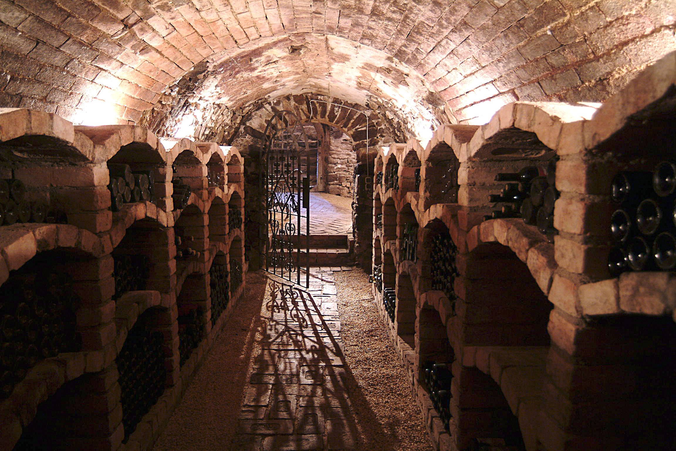 A wine cellar with brick vaults and wine bottles on shelves.