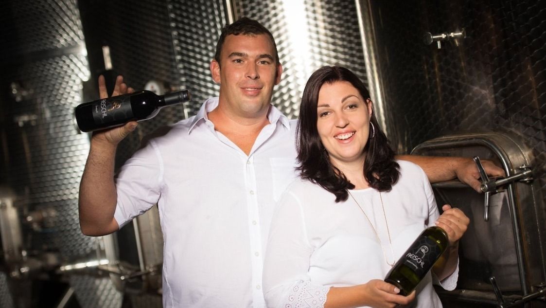 A winemaker couple in the wine cellar with bottles of wine in their hands.