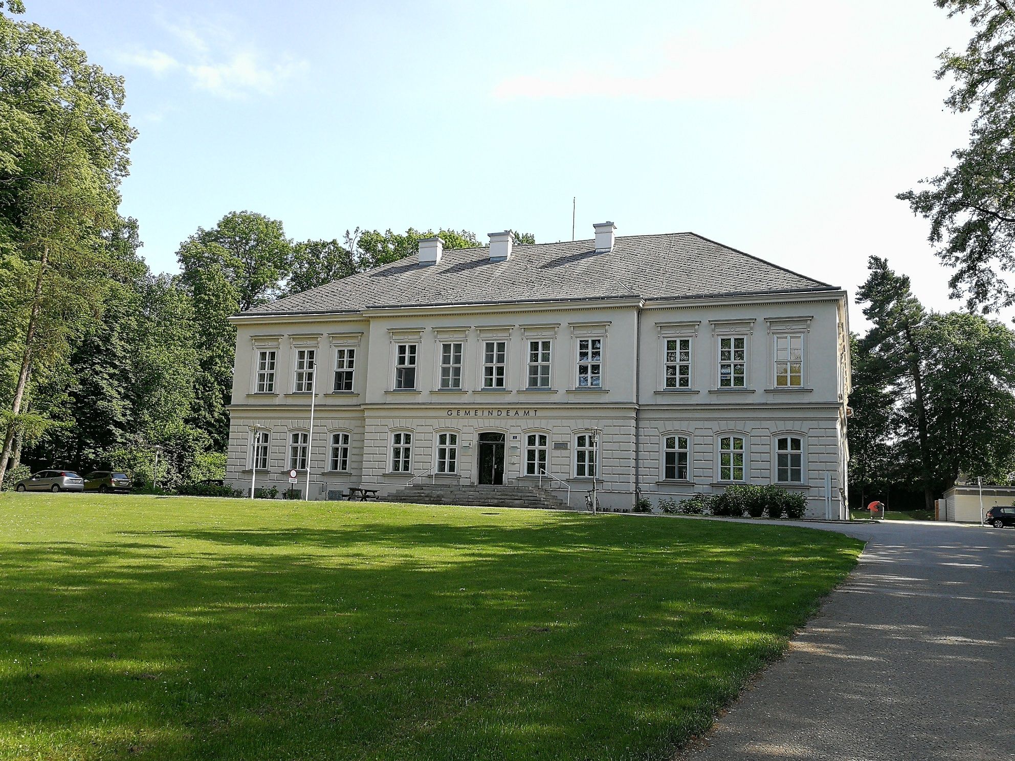 Würmla Castle, a two-storey building with a gray roof and white walls, surrounded by trees and lawns.