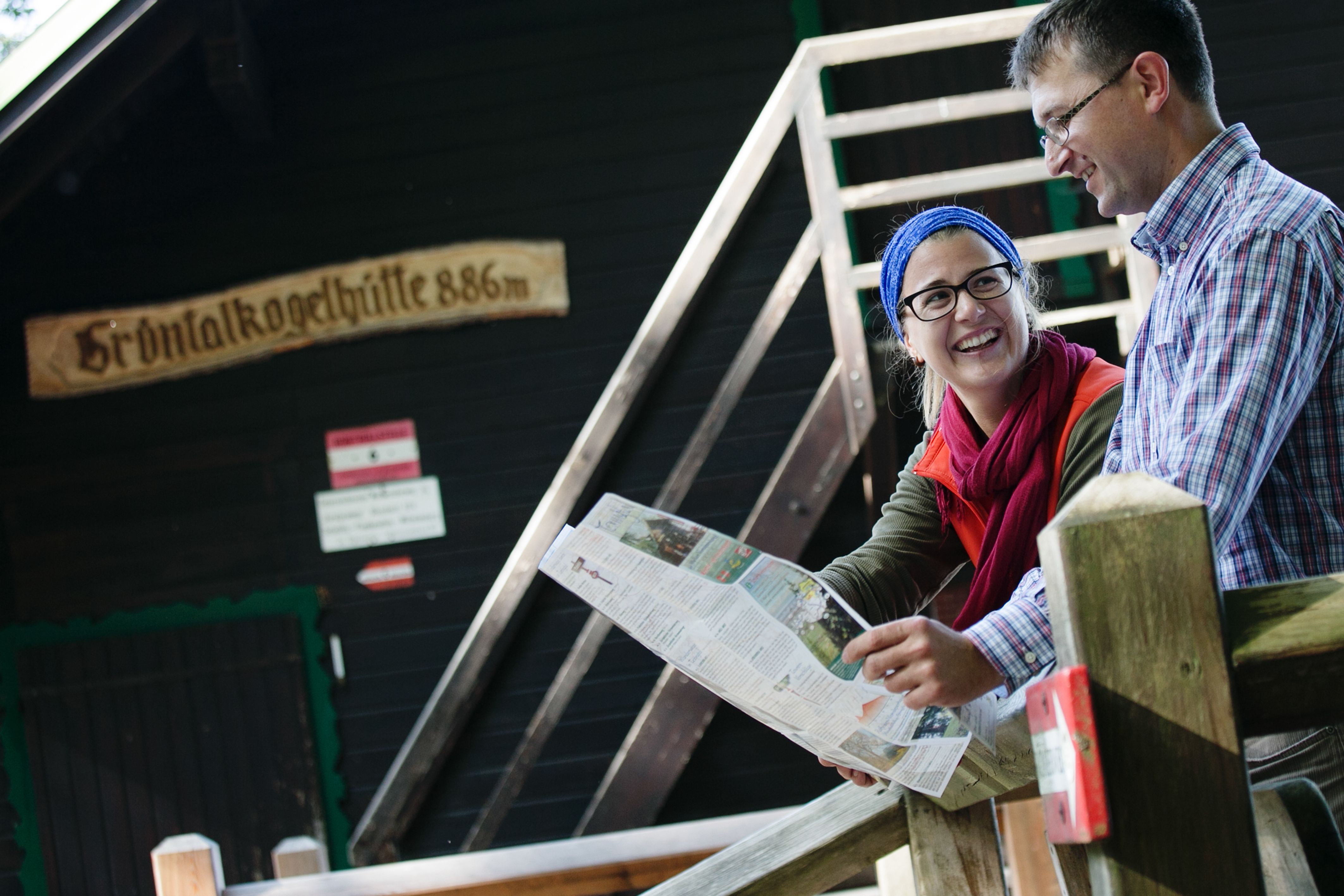 Two people sit in front of the Grüntalkogel hut and look at a map.