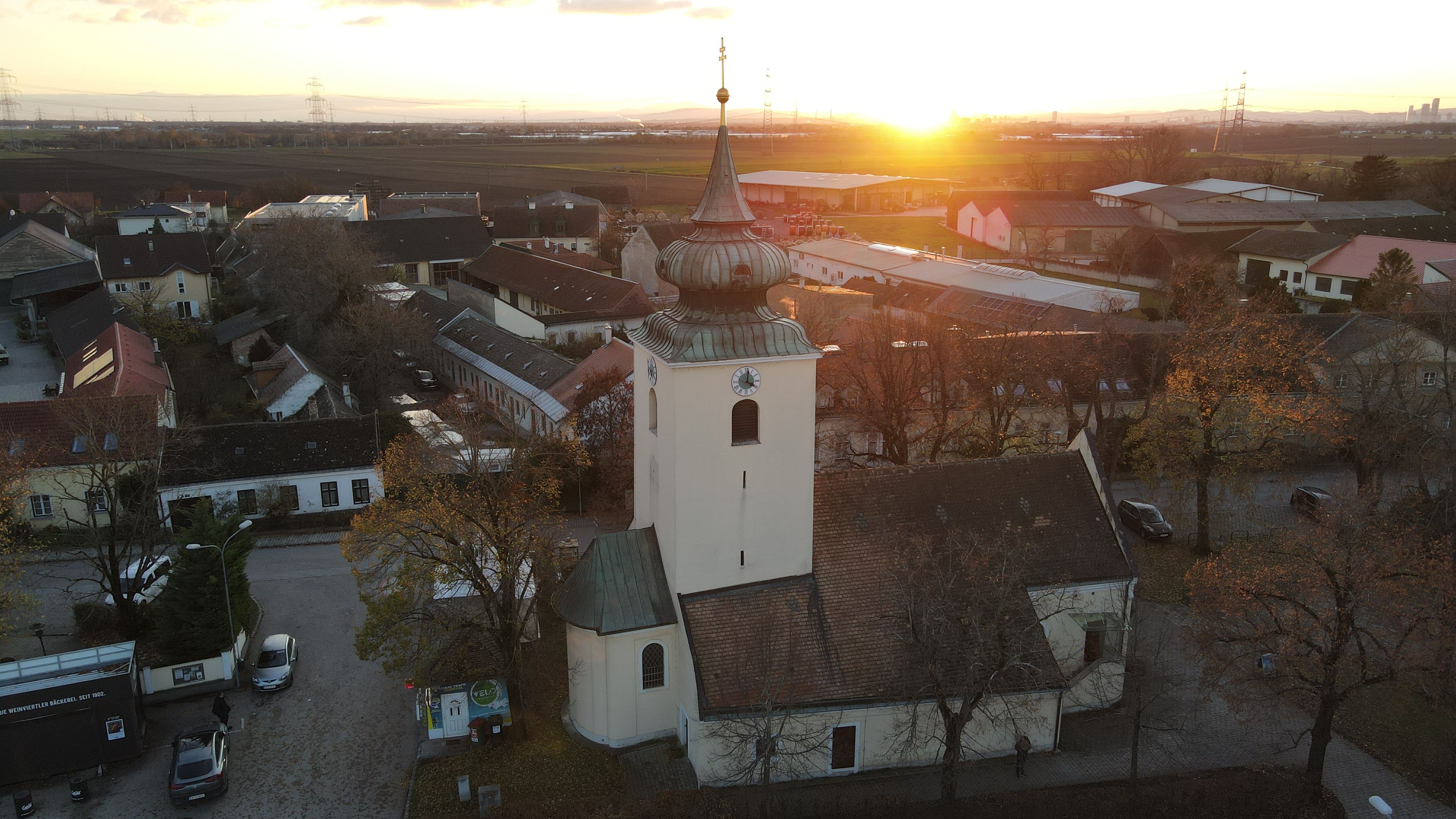 The Raasdorf church, with its tower and onion-domed roof, at sunset, surrounded by houses and fields.