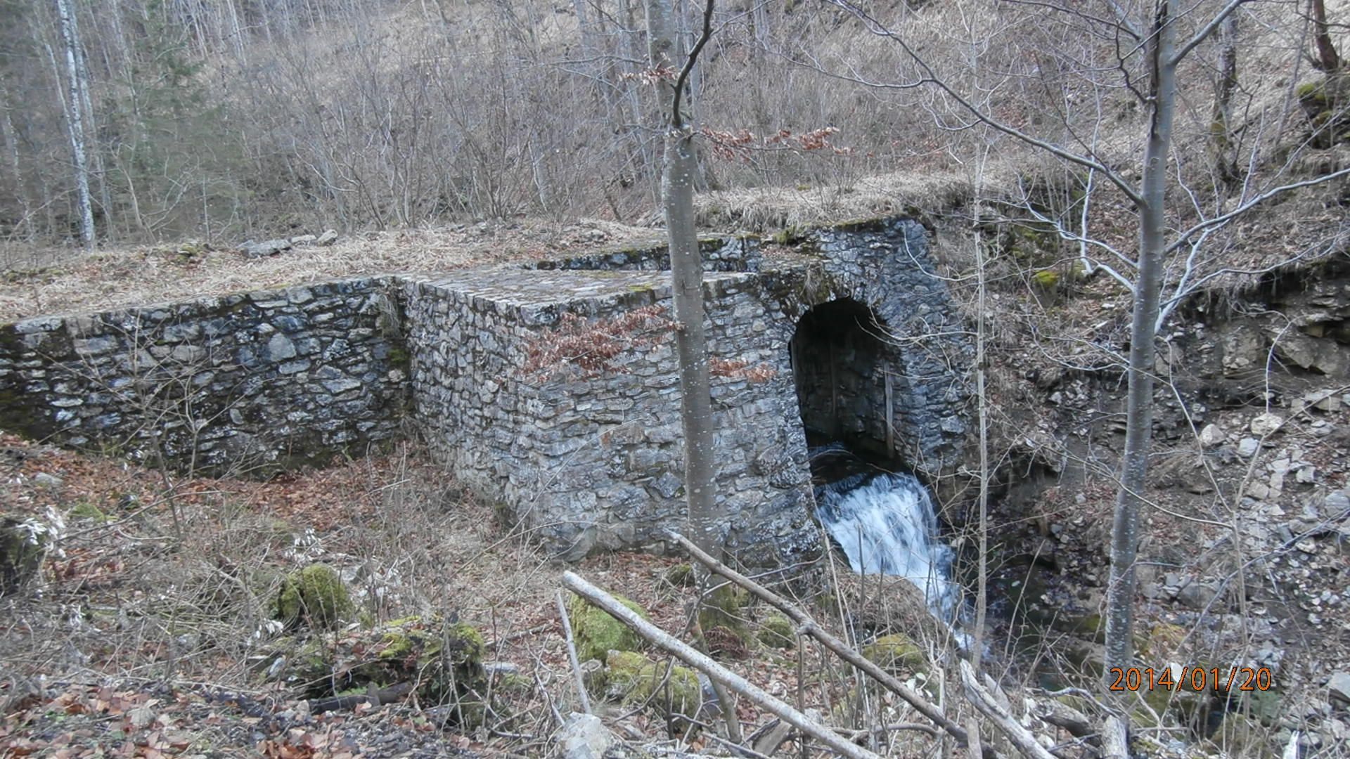 Stone wall with waterfall in wooded surroundings.