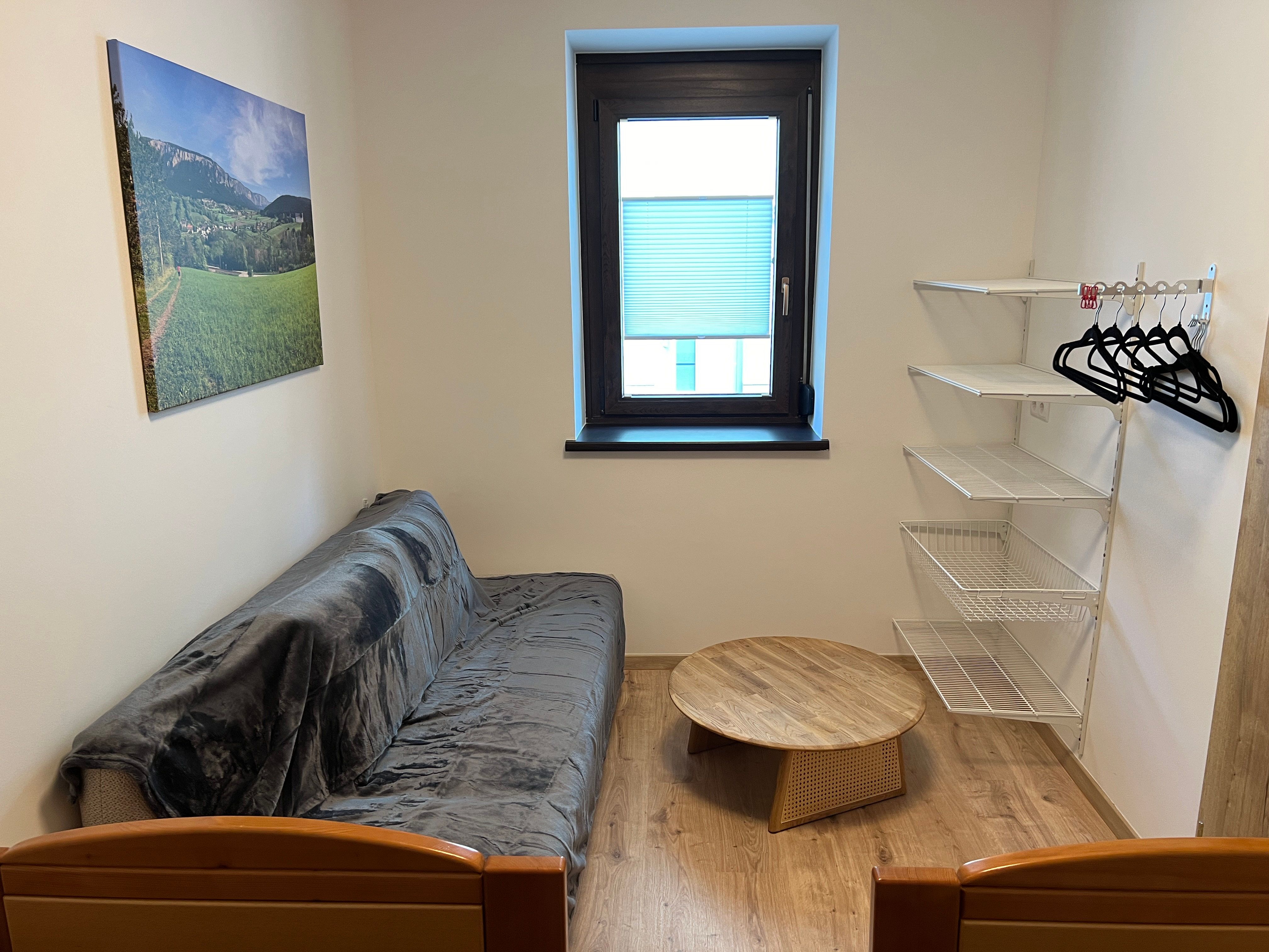 Small room with sofa, round wooden table, wall shelf and window.