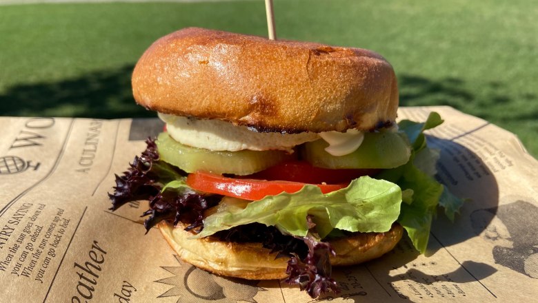 A burger with lettuce, tomatoes and gherkins on a tray outside.