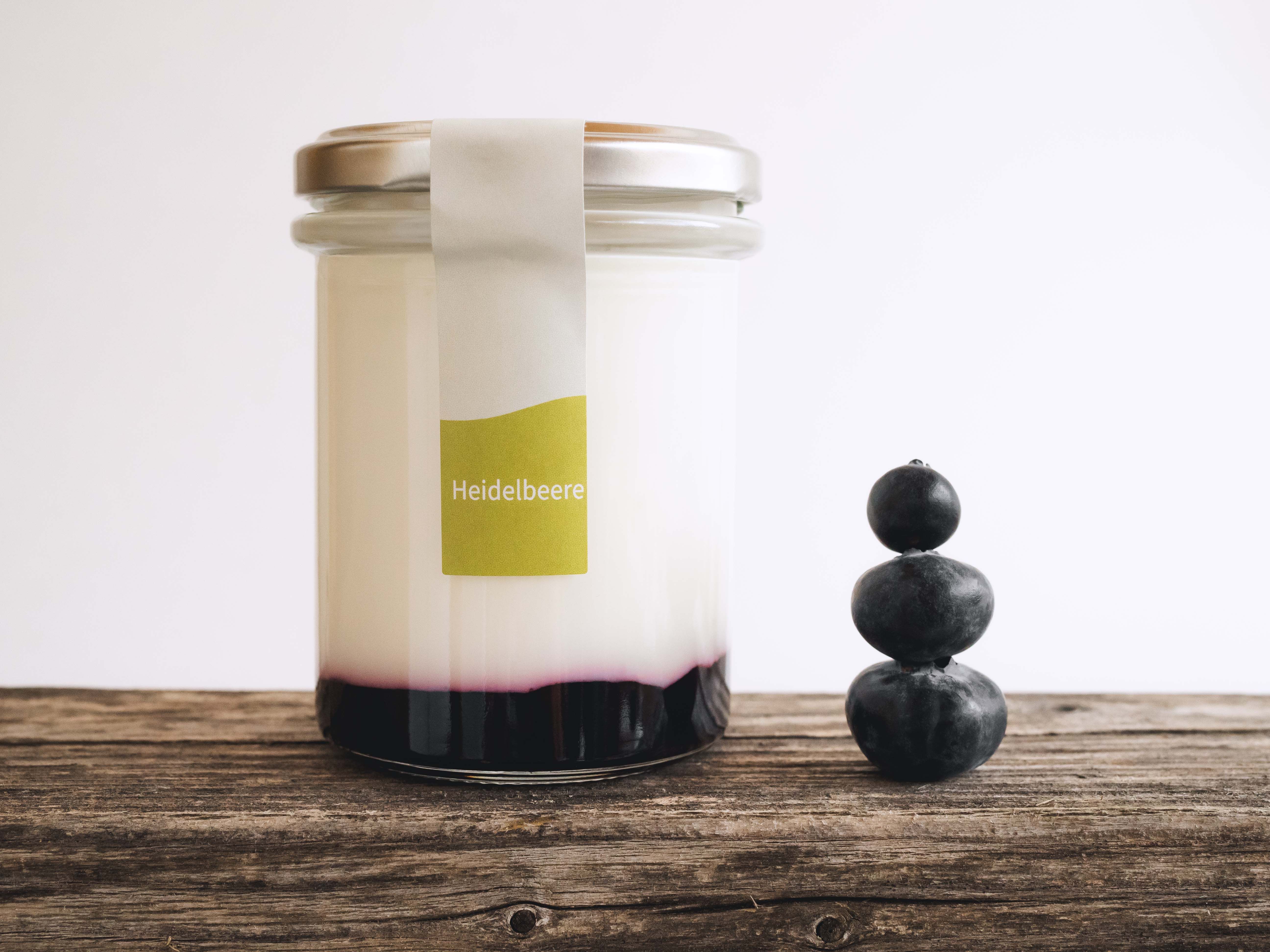 A glass filled with yogurt and fruit on a wooden table, next to it 3 stacked blueberries.