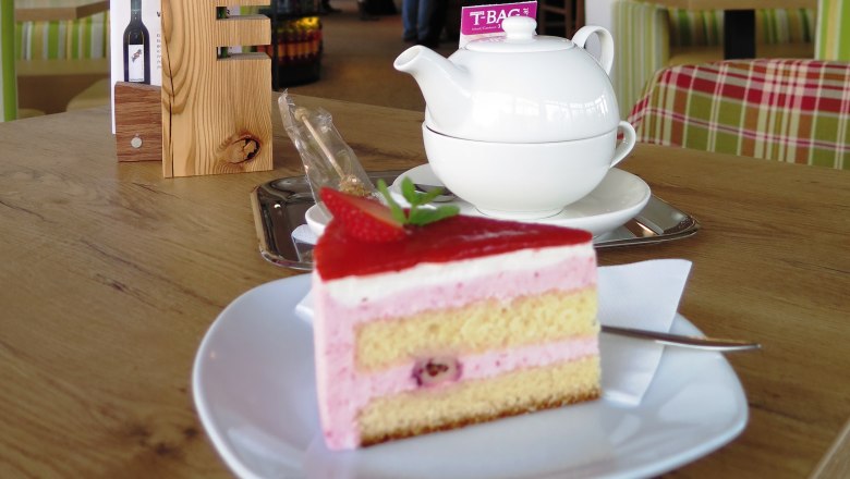 A slice of strawberry cake on a plate with a teapot in the background on a wooden table.