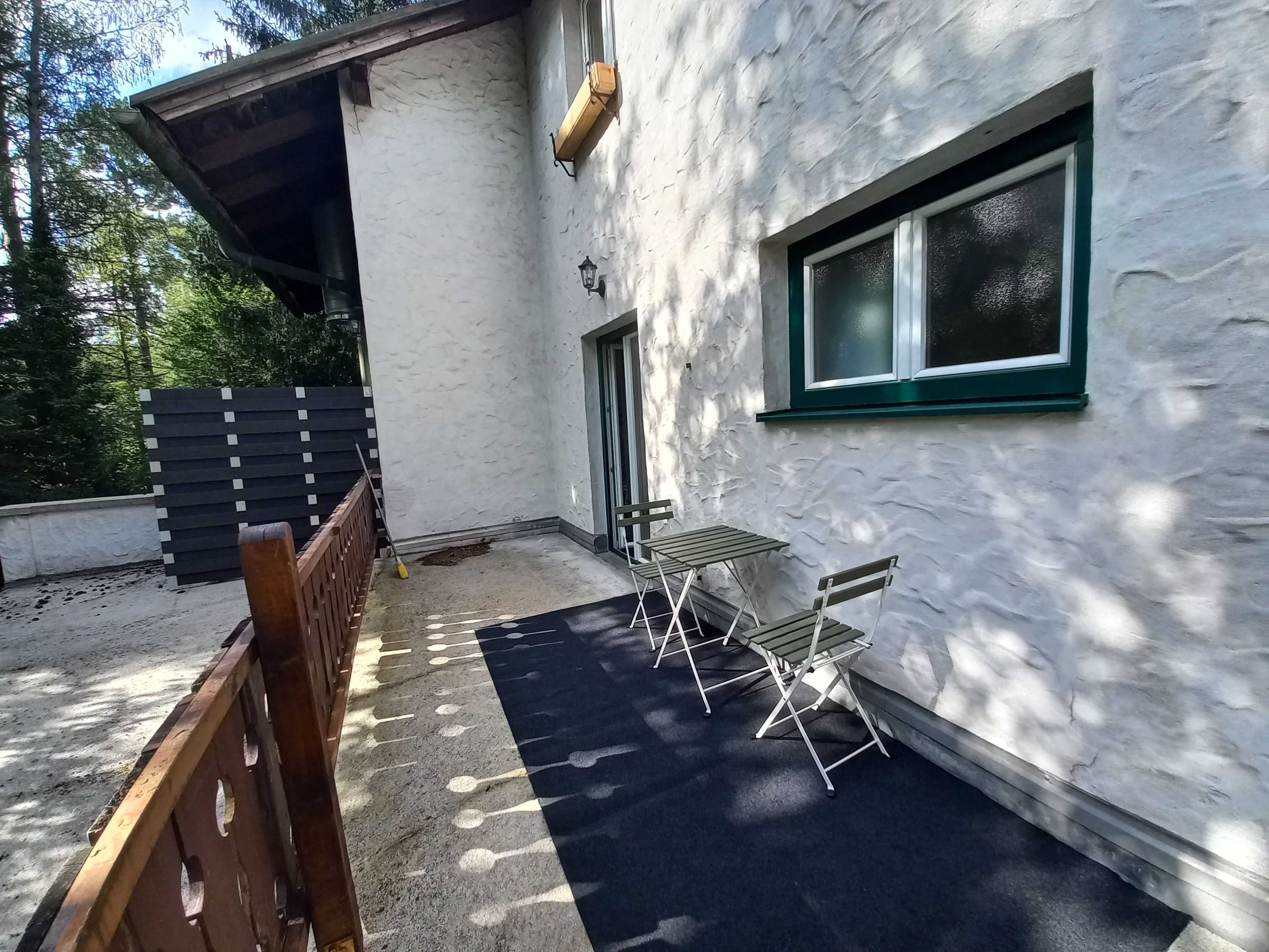 Terrace of a vacation apartment with table and chairs, surrounded by trees.