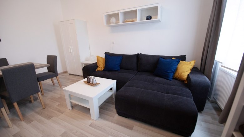 Modern living area with grey sofa, colorful cushions, white coffee table and dining table with chairs.