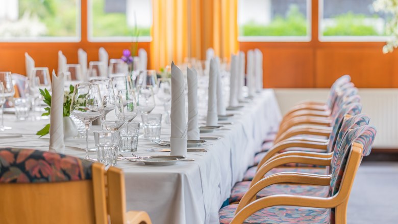 Elegantly laid table in a conservatory with white napkins, glasses and cutlery. Large windows in the background.