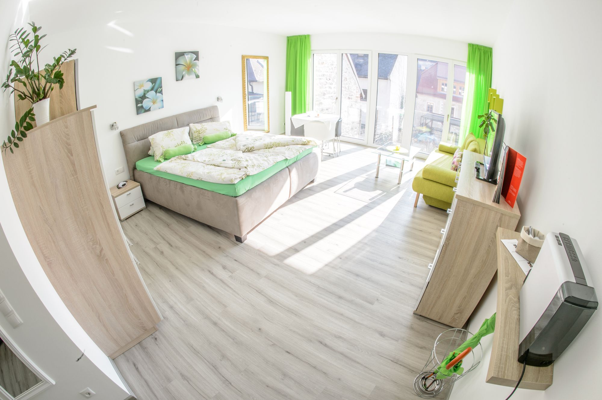 Bright guest room with double bed, sofa, TV and large windows.