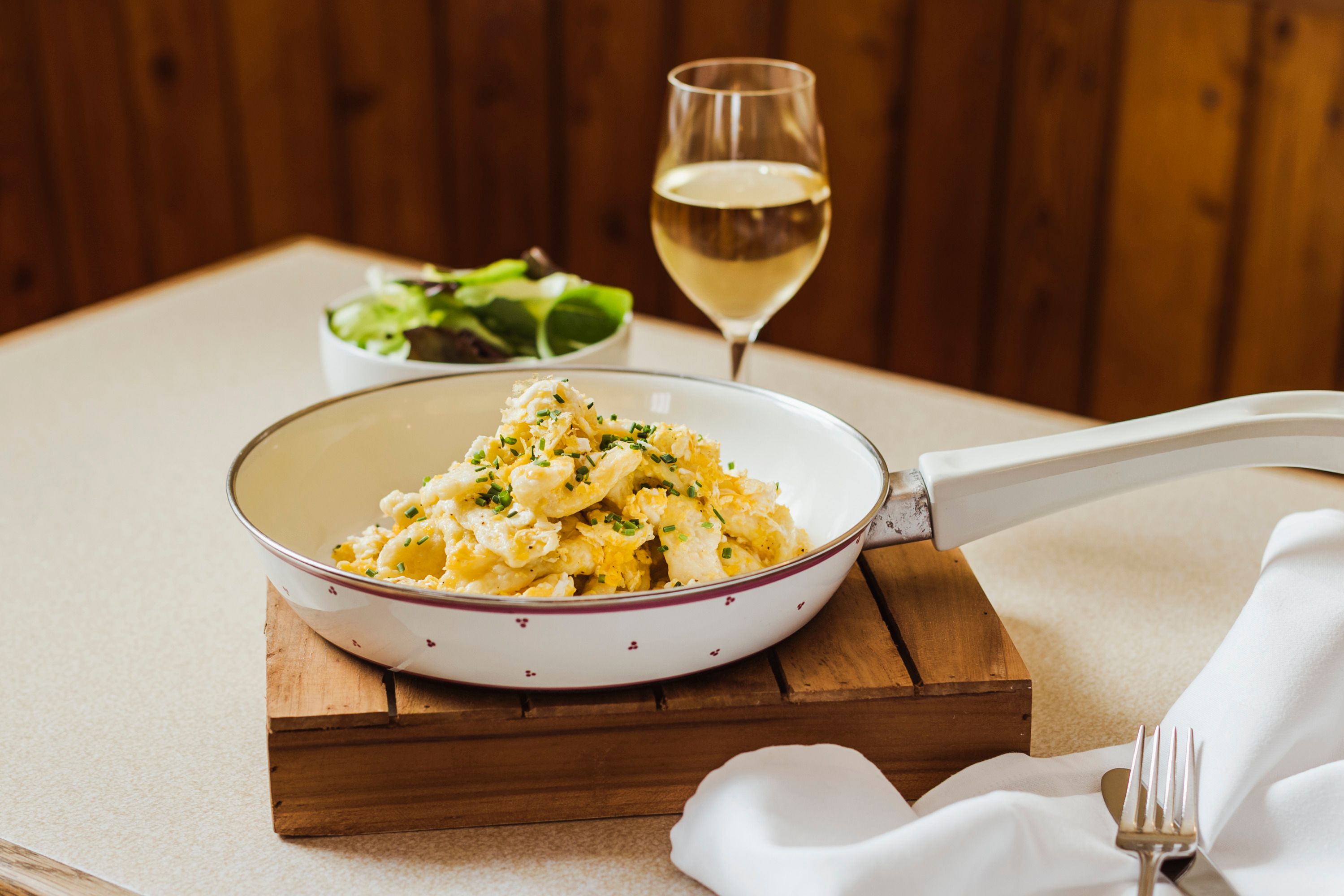 Egg dumplings in a pan with a glass of white wine and a salad in the background.
