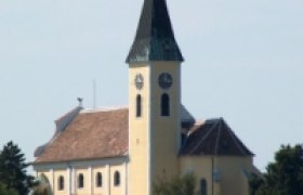 Großebersdorf parish church with pointed tower and clock, surrounded by trees.