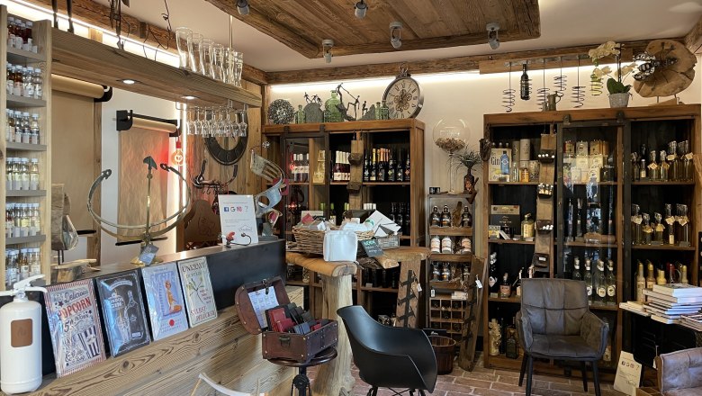 A cozy store with rustic wooden furnishings, shelves full of products and decorations. There are books, bottles and seating.