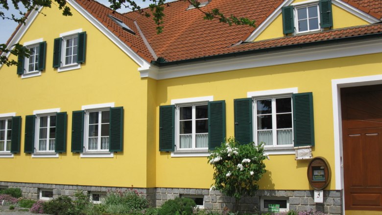 Yellow house with green shutters and red tiled roof.