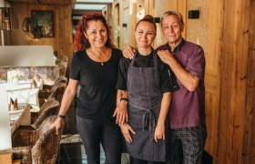 Three people in a cozy restaurant, smiling and friendly.