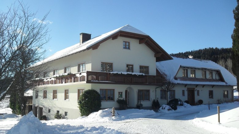 A large farmhouse covered in snow in winter, under a blue sky.
