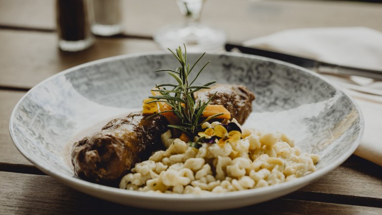 A plate of beef roulade, spaetzle and vegetables, garnished with rosemary and edible flowers.