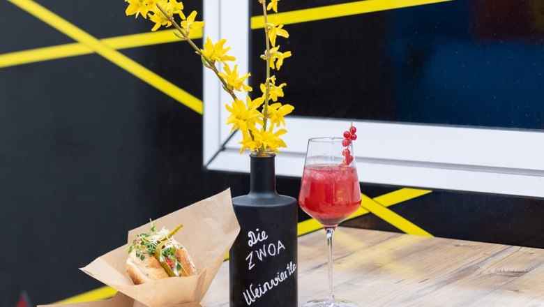 A drink and a sandwich on a table with a vase of yellow flowers.