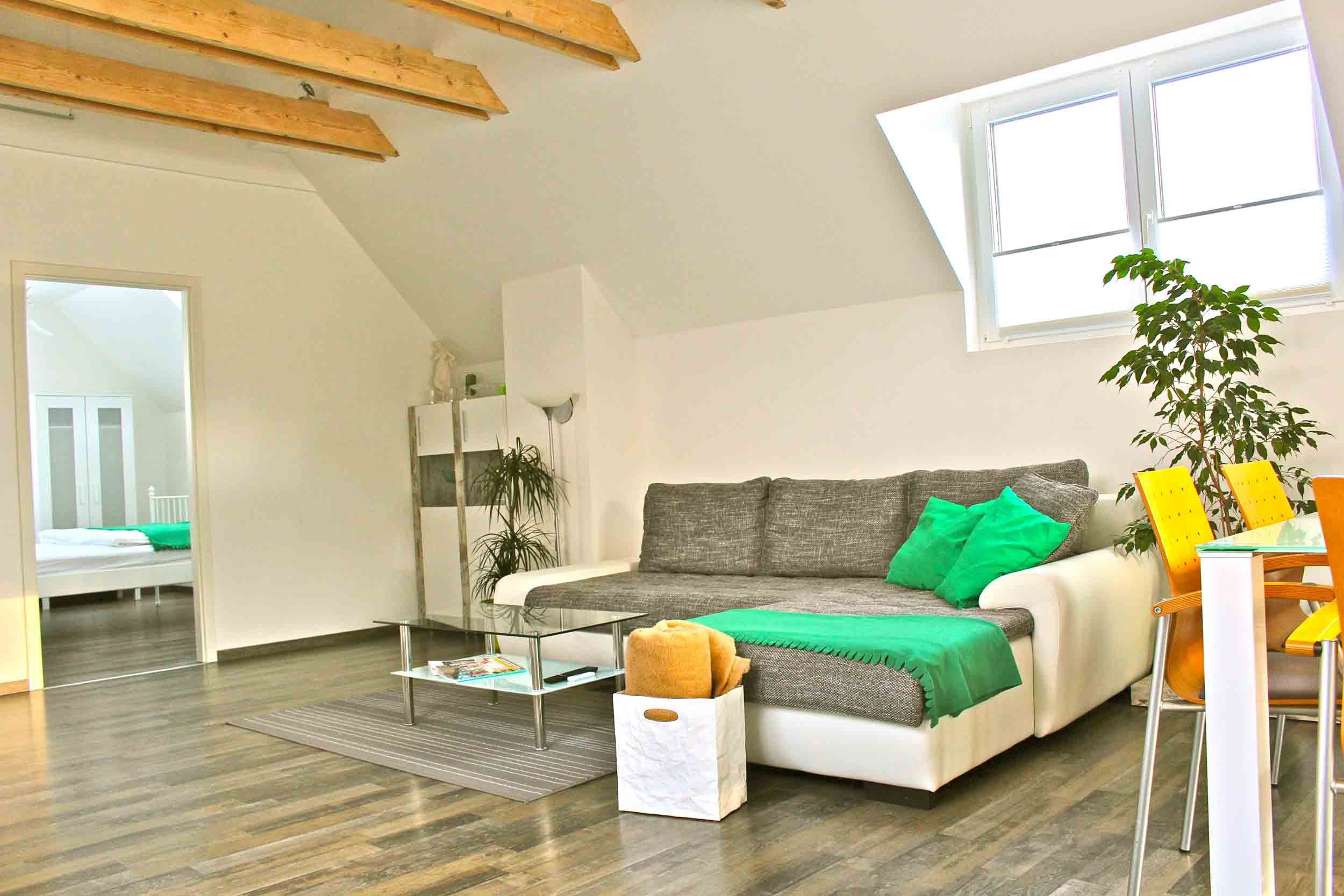 Bright living room with gray sofa, green cushions, glass table and dining area with yellow chairs.