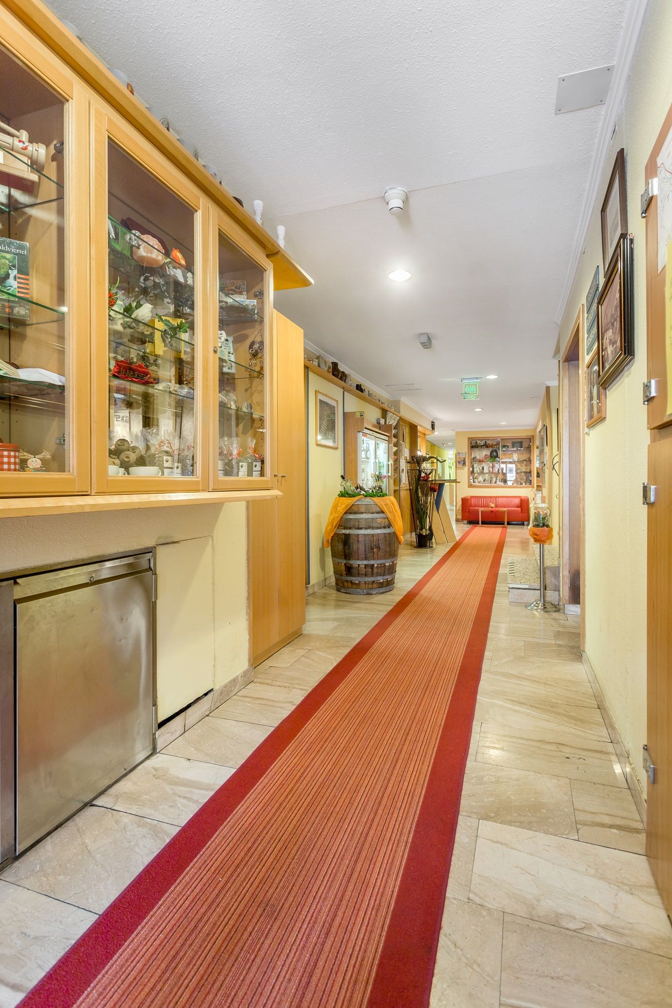 A hotel corridor with red carpet, showcases and decorations.