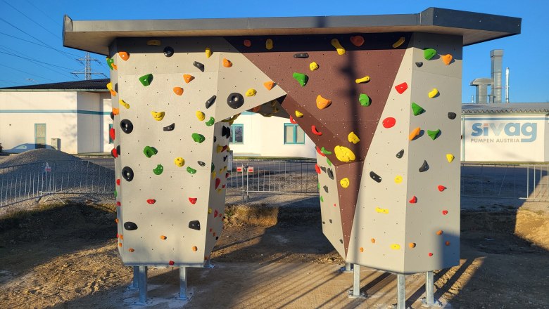 A free-standing bouldering wall with colorful climbing holds on a sunny site.