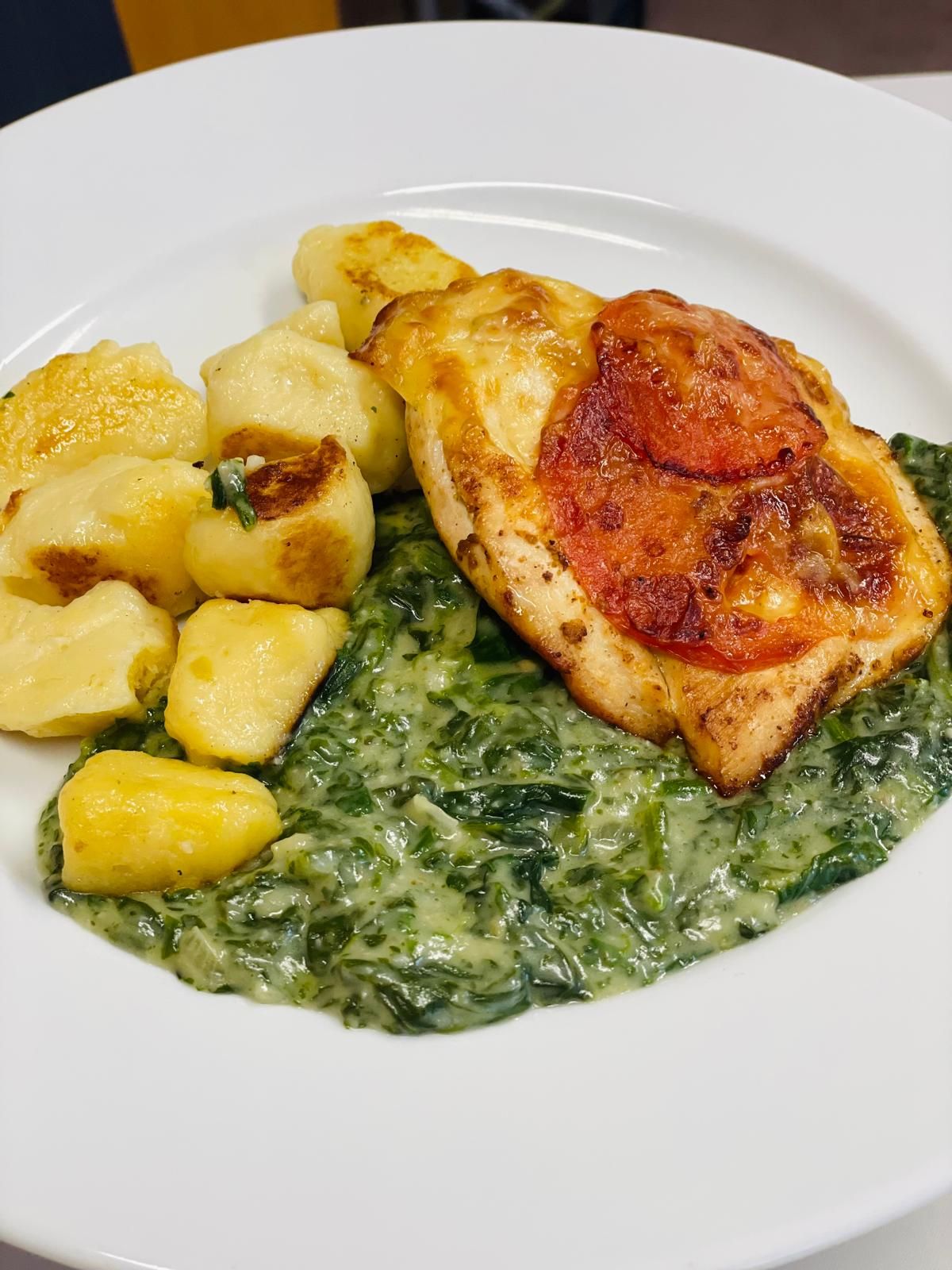 A plate of gnocchi, creamy spinach, and chicken au gratin with a slice of tomato.