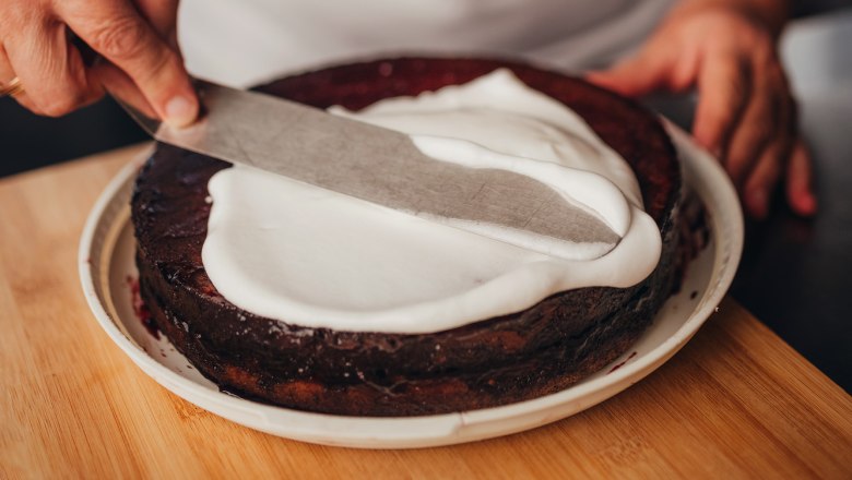 One person spreads white icing on a chocolate cake.
