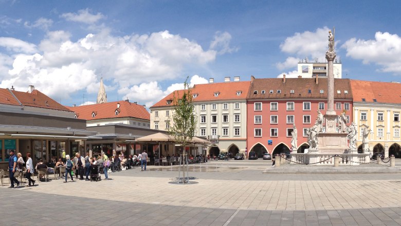 Panoramic view of a lively main square with historic buildings and a statue in the middle.