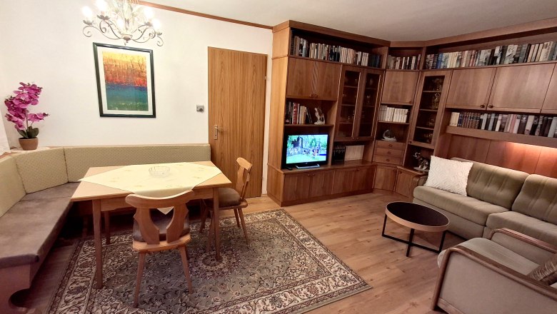 Cozy living area with corner bench, wooden furniture, carpet and TV.