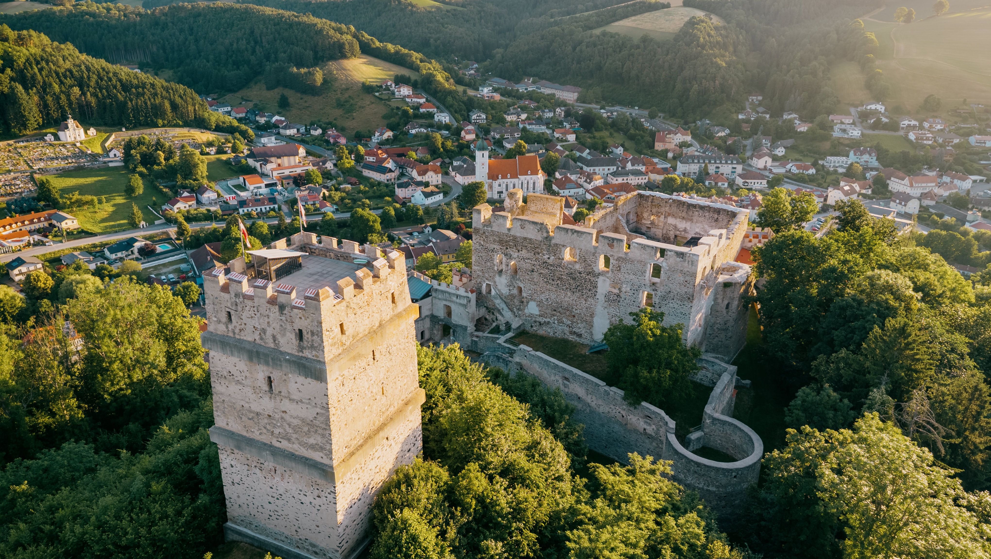 Aerial view of the ruins of Kirchschlag Castle surrounded by green trees and the municipality of Kirchschlag in the background.