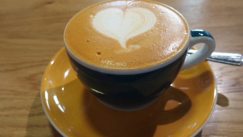 A cup of cappuccino with heart latte art on a wooden table.