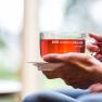 Close-up of hands holding a cup with a red drink on which is written 'DER andere URLAUB KLOSTERBERG'.