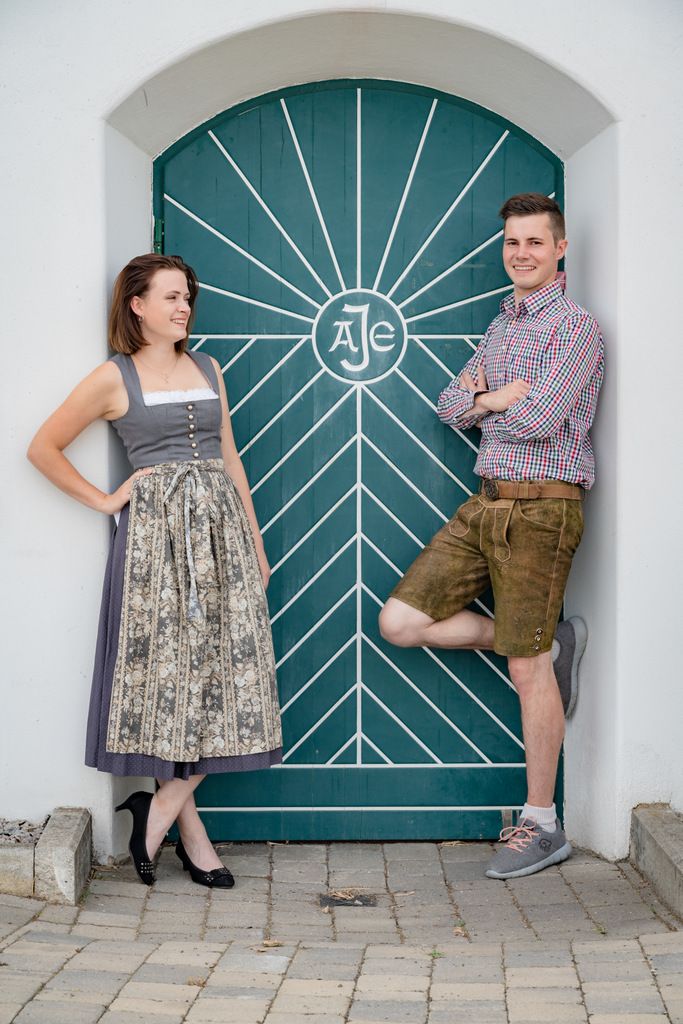 A man and a woman in traditional dress in front of a green door with a geometric pattern.