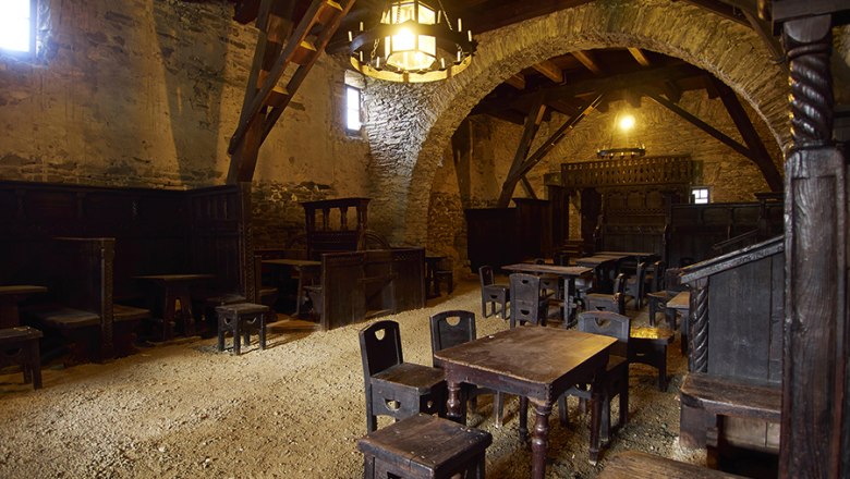 Interior view of a medieval tavern with wooden furniture and stone walls.