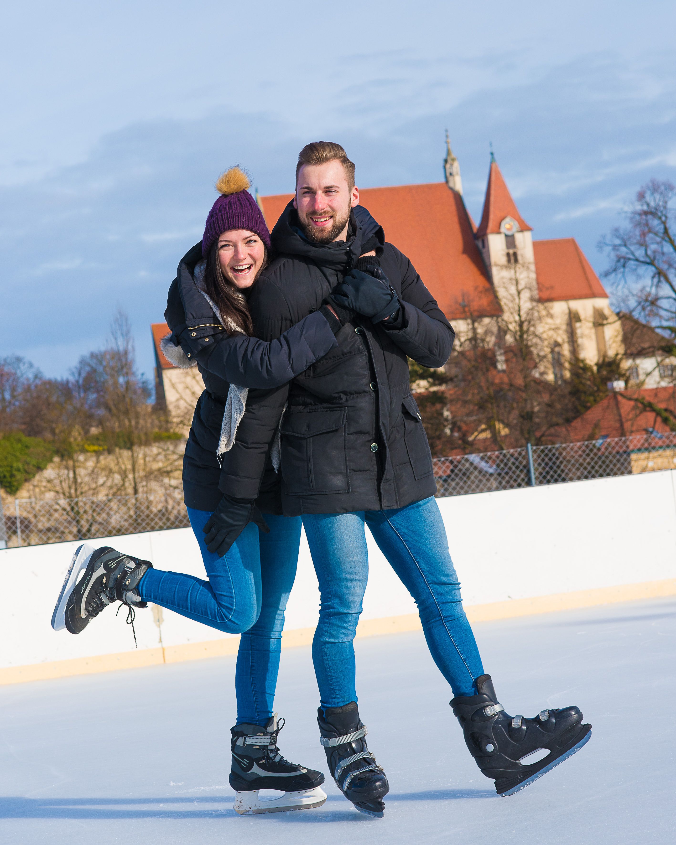 A couple on an ice rink, in the background a church with a red roof.
