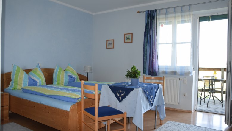 Guesthouse Kalchhauser, © Kalchhauser Cozy guest room with double bed, table and chairs, blue curtains and access to a balcony with seating.